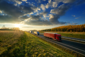 Three trucks driving on a highway in autumn landscape at sunset with dramatic clouds