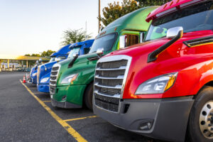 Bright different big rigs semi trucks standing in row on truck stop parking lot