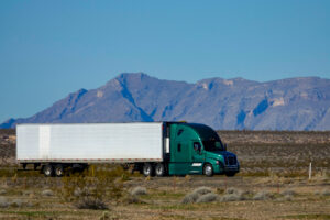 CLOSE UP: Cool shot of barren landscape surrounding a green semi trailer truck.