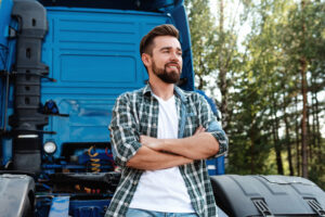 Young smiling male truck driver beside his blue cargo truck