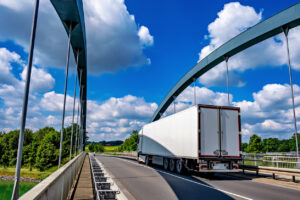 White truck driving down highway bridge over river