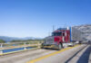 Burgundy big rig classic semi truck with refrigerated shiny semi trailer transporting commercial cargo on the Bridge of God in Columbia River Gorge