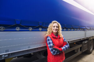 Portrait of female trucker with crossed arm proudly standing by her truck vehicle ready for transportation service.