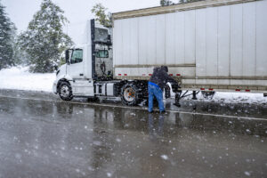 Truck driver puts chains on the wheels of the big rig semi truck with semi trailer to drive safely on a winter highway during a snow storm in the Lake Shasta region in California