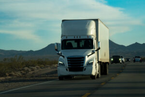 A white semi truck glided through the Nevada Desert, with the majestic mountains standing tall in the backdrop. The setting sun cast a golden glow, painting the scene with breathtaking beauty.