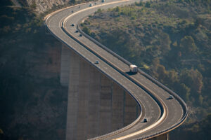 Huge curved viaduct crossing a ravine with a refrigerated semi trailer truck and several vehicles driving along the road, elevated view.