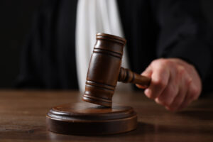 Judge with gavel sitting at wooden table against black background, closeup