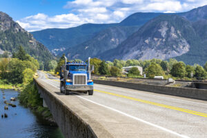 Blue tipper big rig semi truck with tip trailer running on the transportation bridge across the river in Columbia Gorge