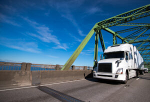 Big rig white semi truck with dry van trailer transporting commercial goods to destination warehouse along the bridge