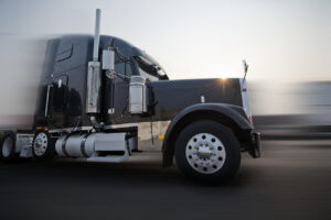 Profile of dark bonnet classic big rig semi truck going on the road with sunshine