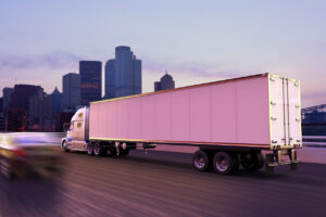 A cargo truck on the road at dusk in front of a city skyline.