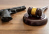 Crime, gun carry and use punishment concept. Judge gavel and handgun on table, close up