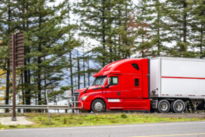 Fire red big rig semi truck transporting cargo in dry van semi trailer running on the road along the Columbia river