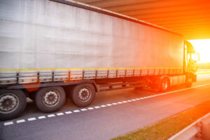 A truck with a semi trailer drives under a bridge against the backdrop of sunset. The concept of work and rest among truck drivers, industry