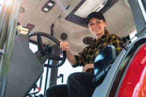 Low angle portrait of a woman sitting in the cab of a tractor. Agricultural and construction dealership, machinery leasing service.