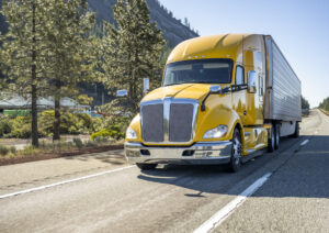 Bright yellow bonnet industrial big rig semi truck transporting cargo in refrigerator semi trailer running on the highway road with rest area on the side