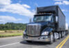 Black day cab big rig semi truck transporting cargo on dry van and flat bed semi trailers driving on the narrow road at sunny day