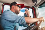 Caucasian Semi Truck Driver In His 30S Taking Conversation Using Cb Radio Inside His Truck Cabin.