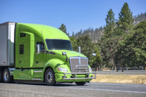 Bonnet green big rig semi truck tractor transporting commercial cargo in dry van semi trailer driving on the one way mountain highway road