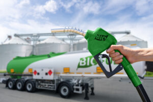 Hand with fuel nozzle with inscription BIO on a background of tank trailer with biofuel. Carbon neutral bio fuel decarbonization concept