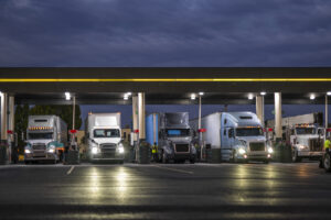 Big rig semi trucks with semi trailers filling truck tanks at a gas station on a truck stop at night time