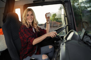 Happy young urban woman holding truck drivers license while siting in truck cabin